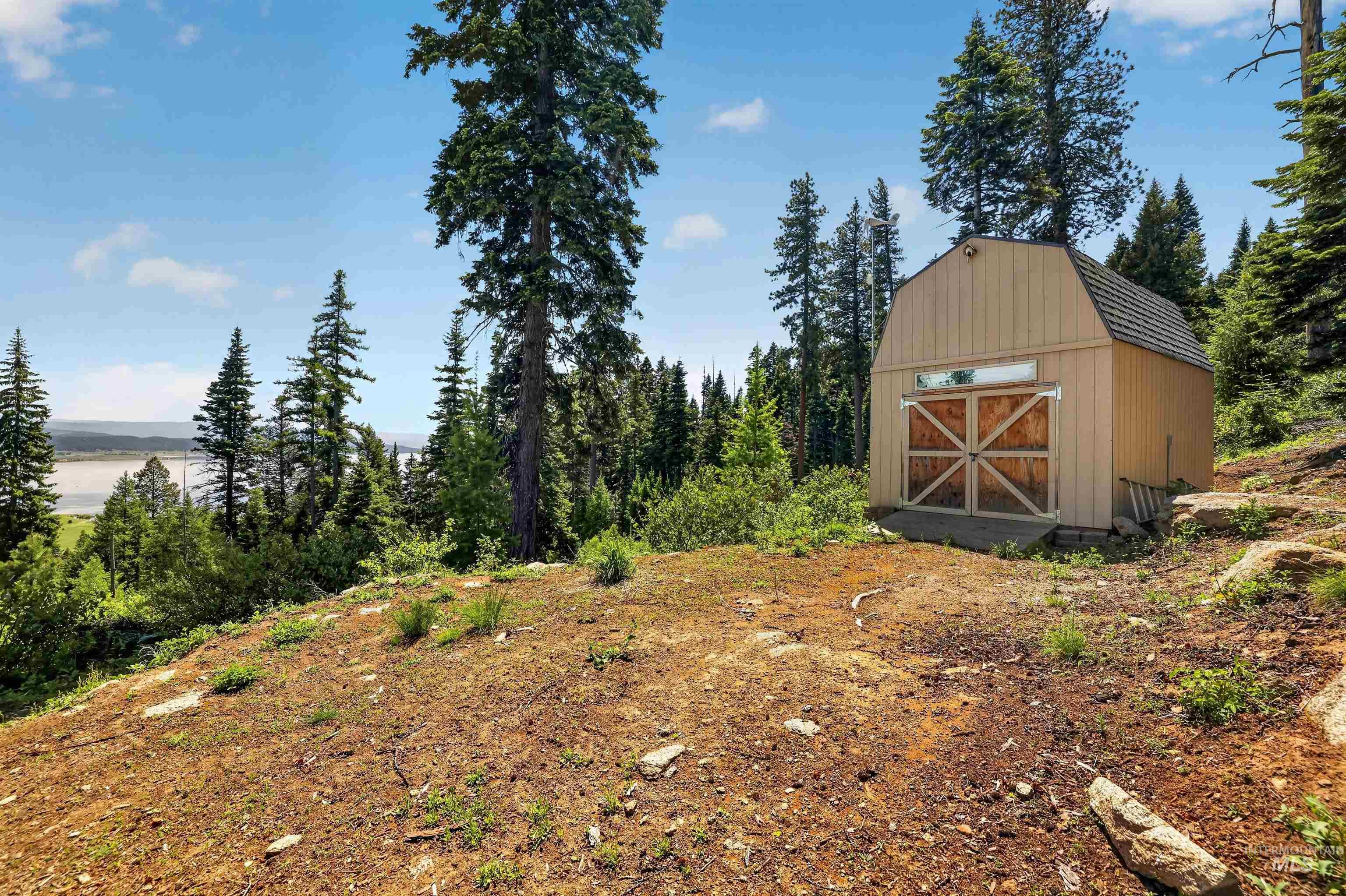 Barn-style shed featuring wood paneling and a shingled roof, surrounded by mature evergreen trees