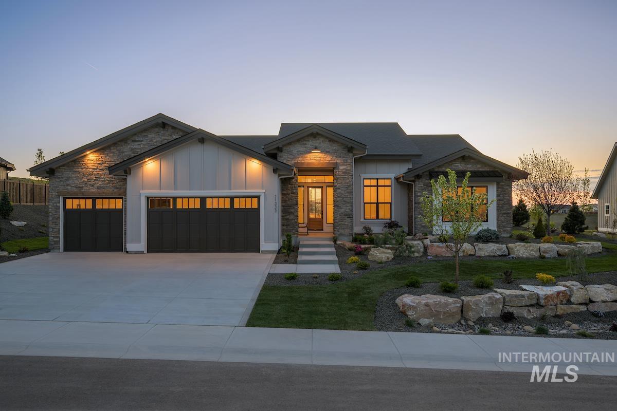 View of front of house with stone siding, a garage, driveway, board and batten siding, and a yard