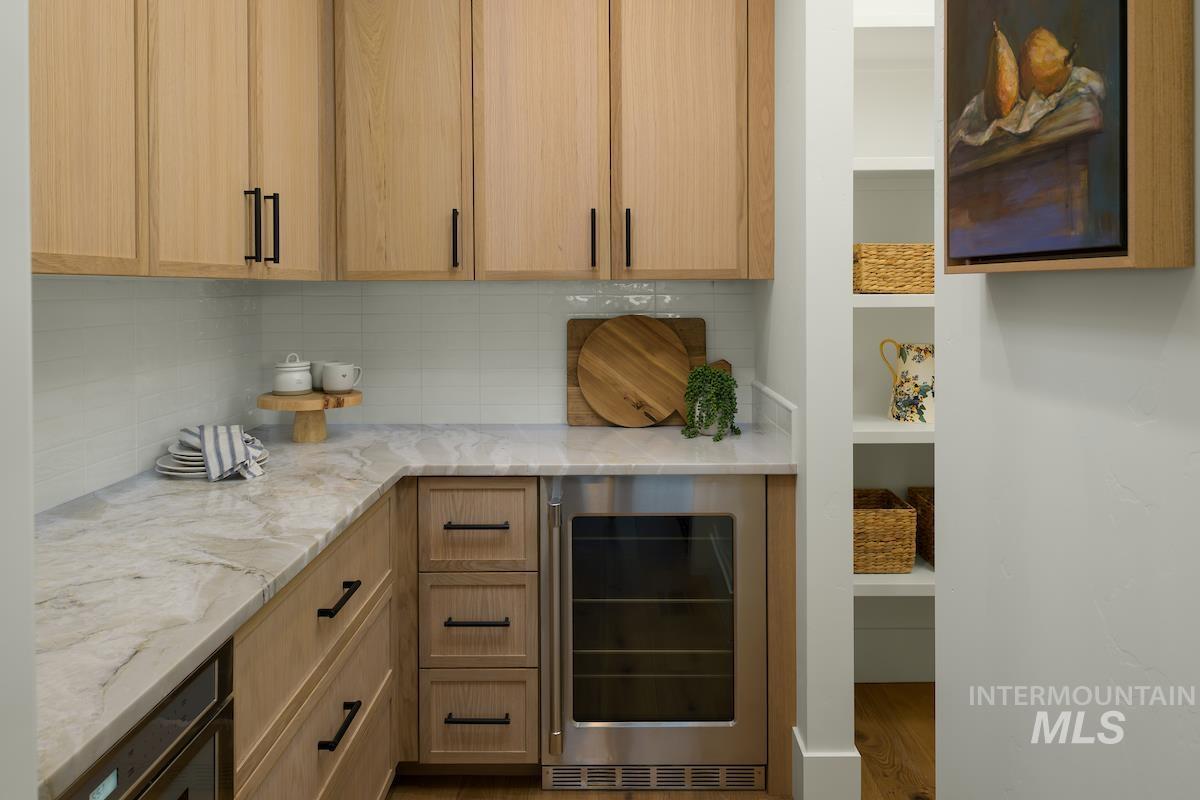 Kitchen featuring beverage cooler, light stone counters, decorative backsplash, and wood finished floors