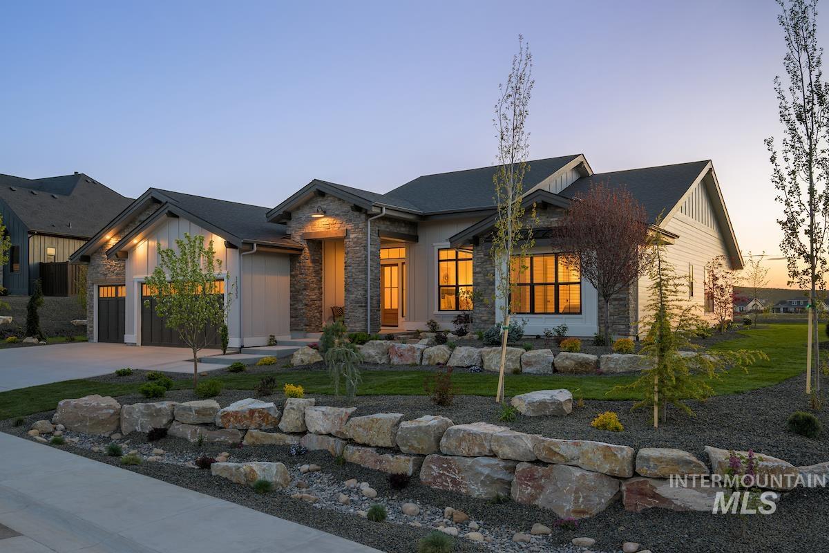 View of front of property with stone siding, an attached garage, driveway, board and batten siding, and a yard