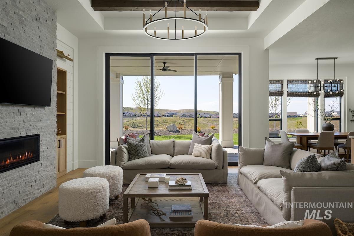 Living area featuring wood finished floors, a chandelier, a fireplace, a raised ceiling, and beamed ceiling