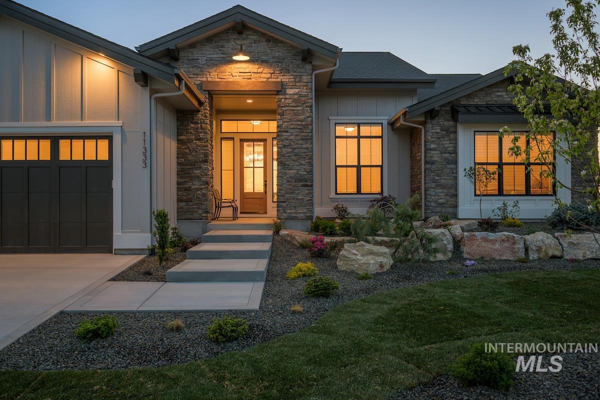 View of front of house featuring an attached garage, driveway, stone siding, and board and batten siding