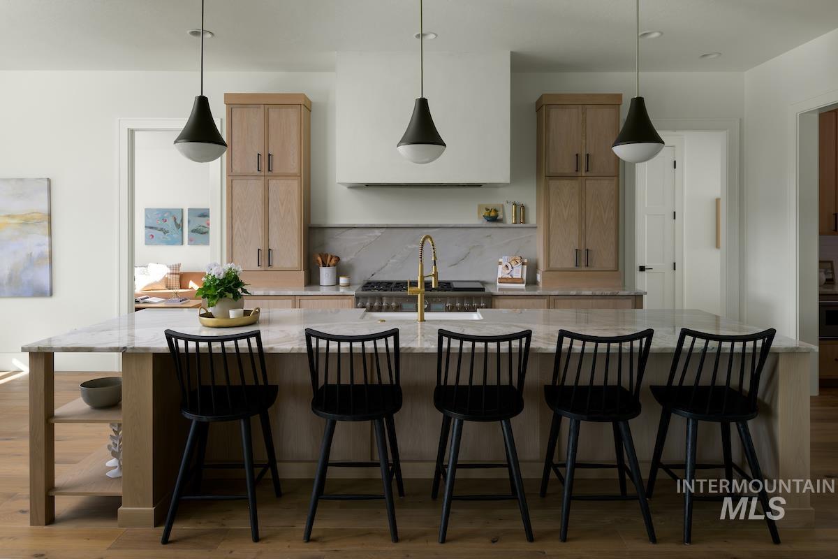 Kitchen with wood finished floors, light brown cabinetry, a large island, and light stone countertops