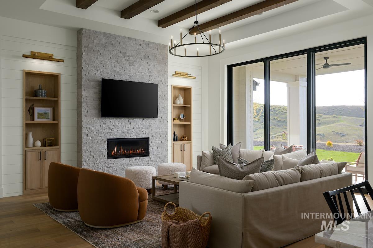 Living room featuring beamed ceiling, built in shelves, a fireplace, a chandelier, and wood finished floors