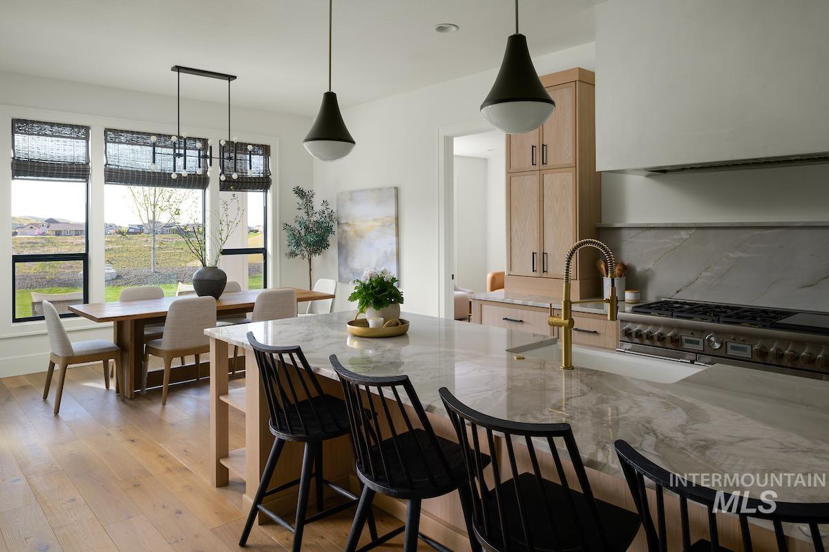 Kitchen with light brown cabinets, high end range, light stone countertops, a kitchen bar, and light wood-style flooring