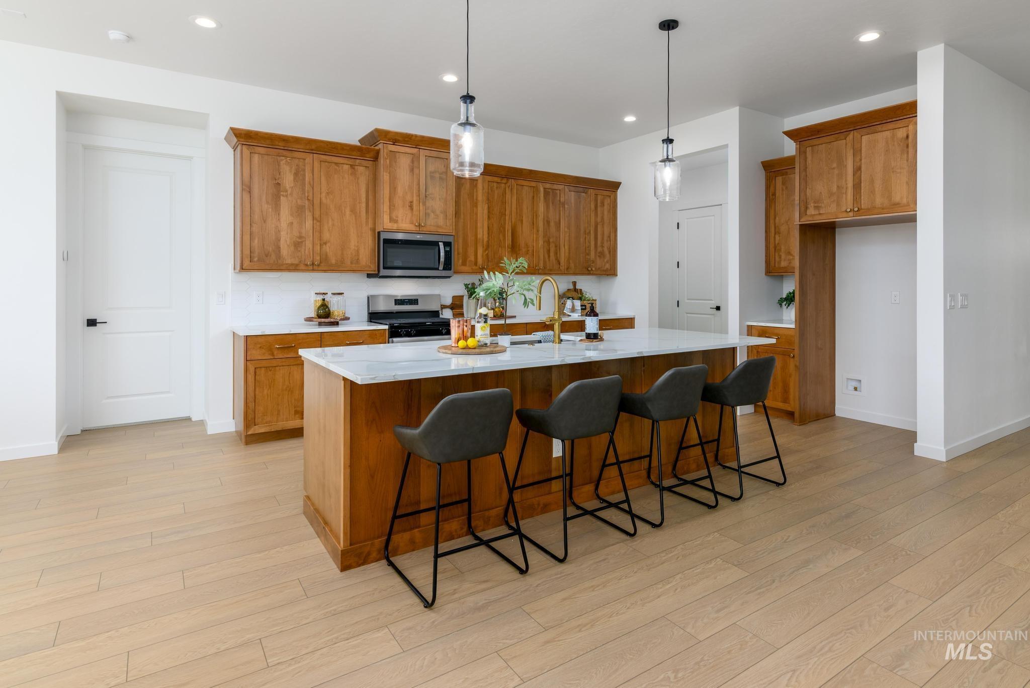 Kitchen with brown cabinetry, a kitchen bar, decorative light fixtures, recessed lighting, and an island with sink