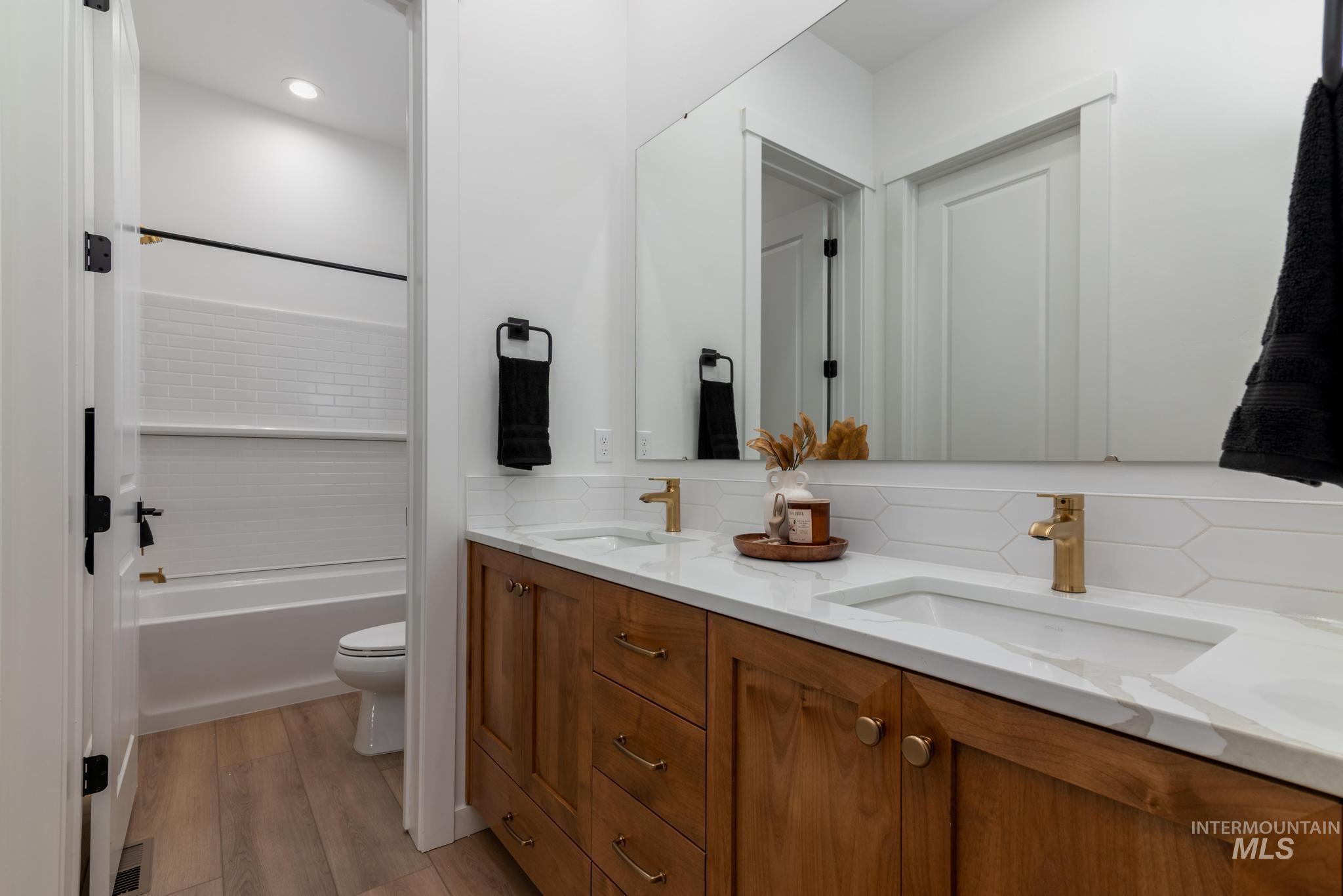 Bathroom with double vanity, backsplash, light wood finished floors, and bathing tub / shower combination