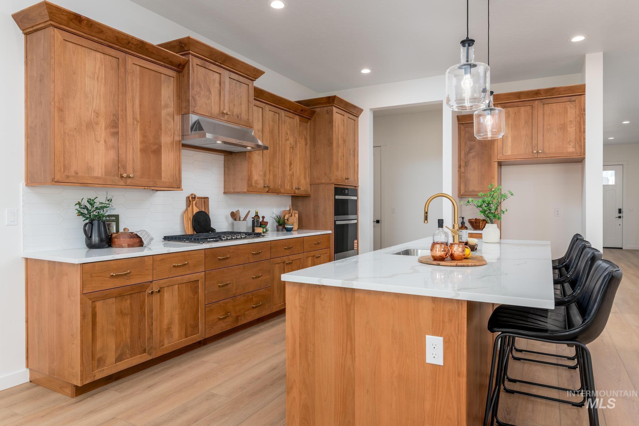 Kitchen with brown cabinetry, a center island with sink, a breakfast bar area, light wood-type flooring, and recessed lighting