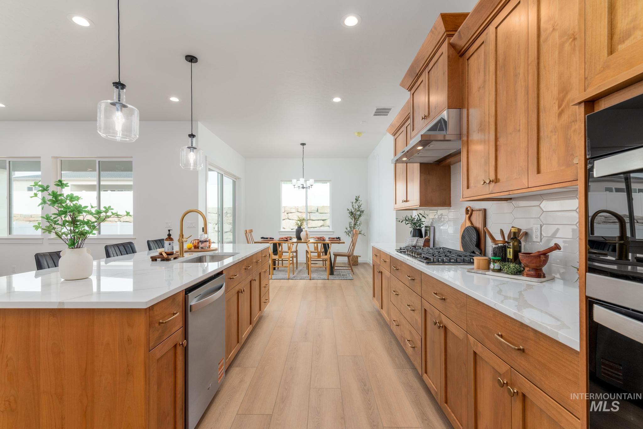 Kitchen with pendant lighting, light stone counters, tasteful backsplash, appliances with stainless steel finishes, and light wood-type flooring