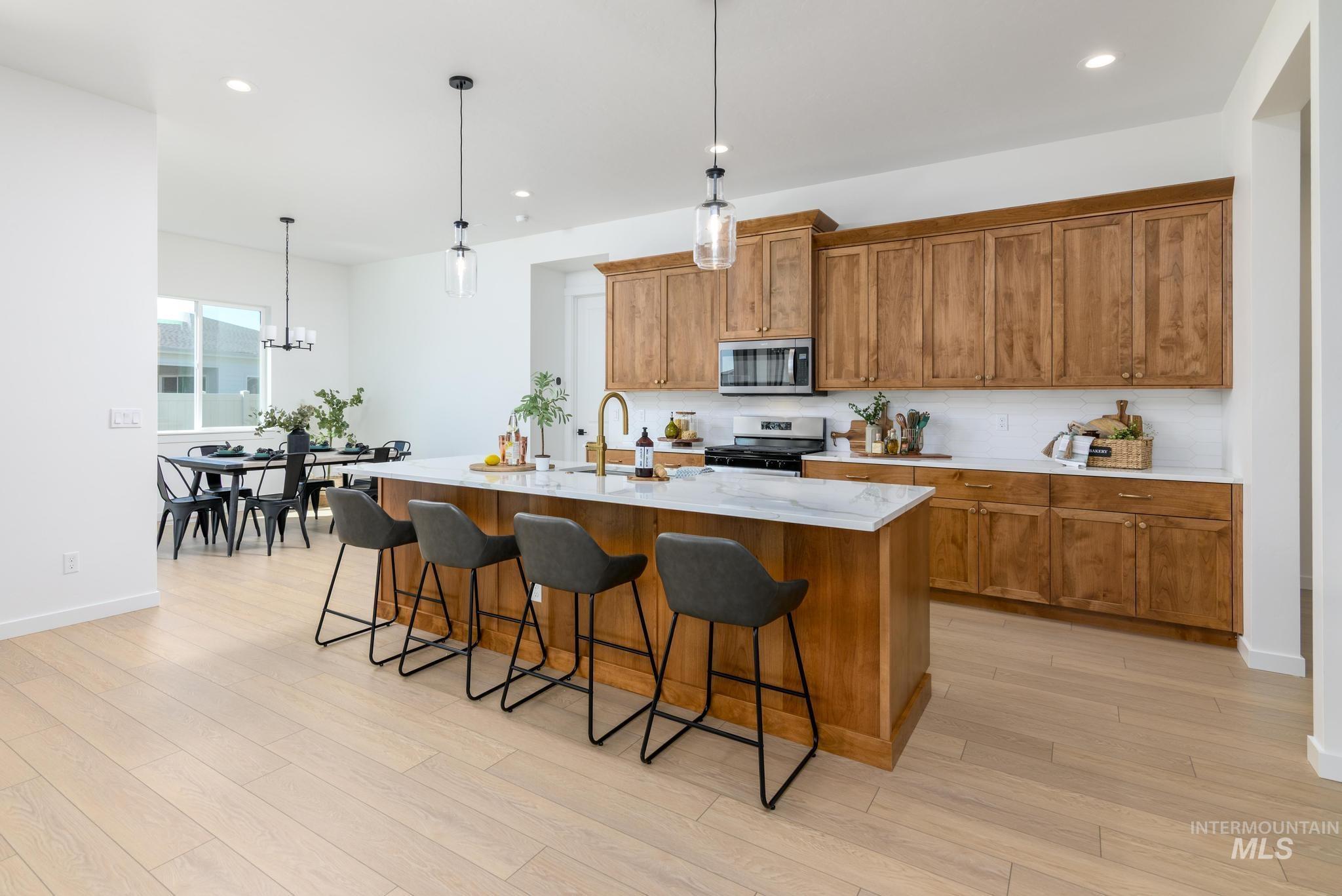 Kitchen featuring brown cabinets, decorative light fixtures, a breakfast bar, a center island with sink, and recessed lighting