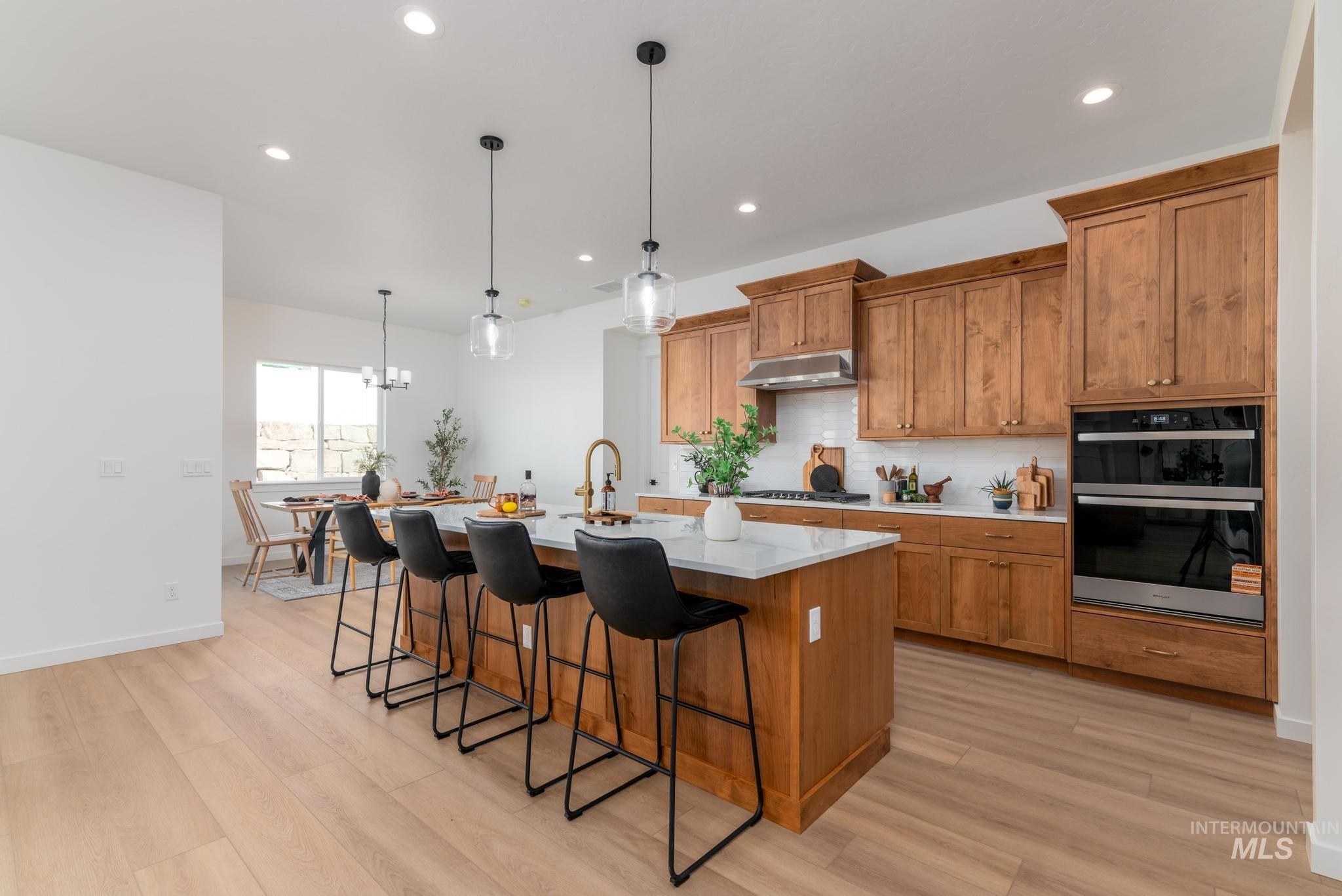 Kitchen featuring brown cabinets, an island with sink, hanging light fixtures, a kitchen breakfast bar, and recessed lighting