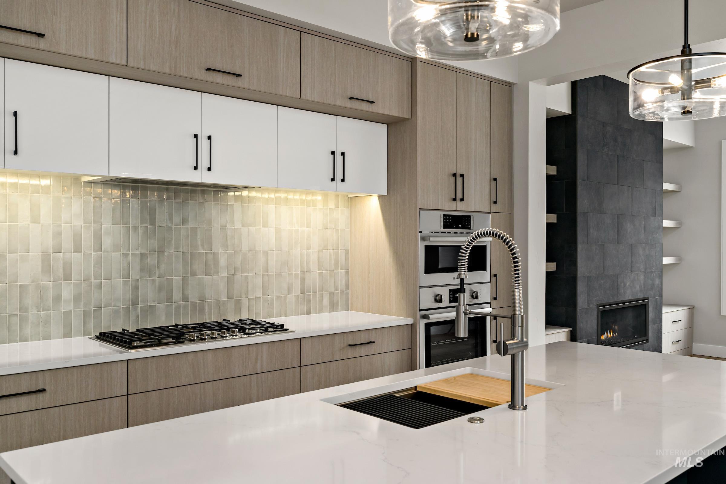 Kitchen with light brown cabinets, decorative backsplash, light stone counters, and hanging light fixtures