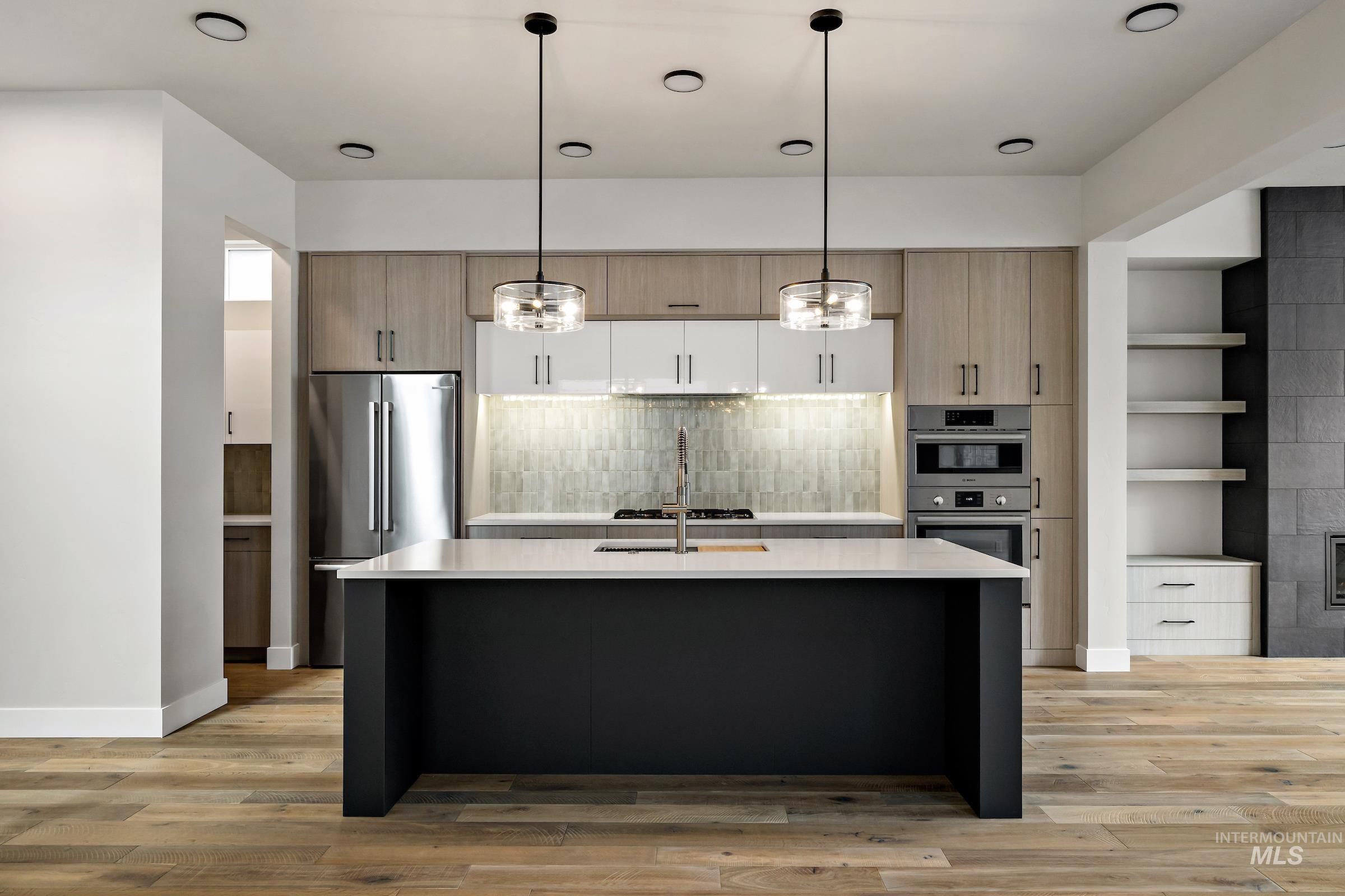 Kitchen featuring decorative light fixtures, appliances with stainless steel finishes, modern cabinets, and light brown cabinetry