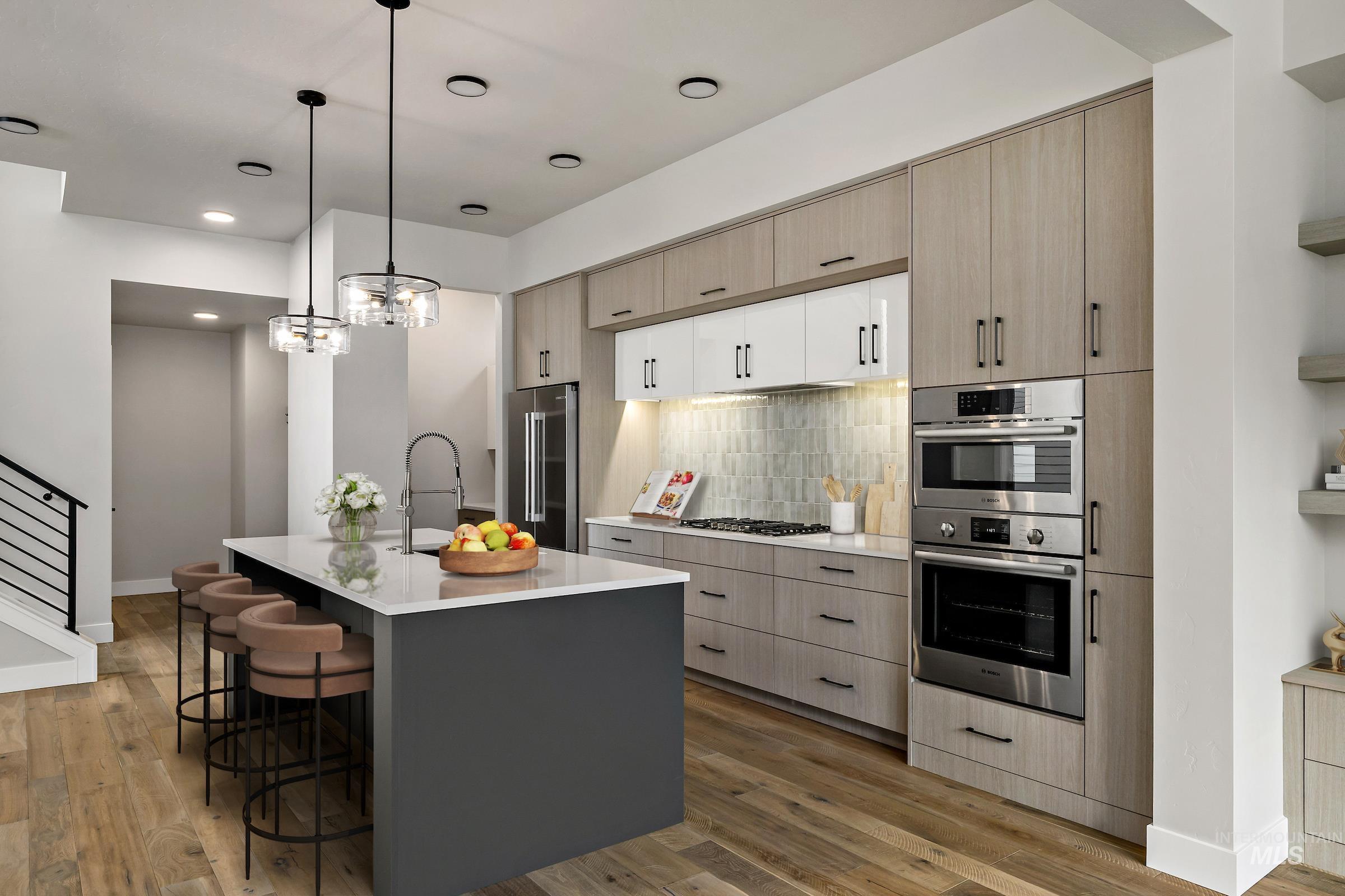 Kitchen with light brown cabinets, decorative light fixtures, a kitchen island with sink, stainless steel appliances, and a breakfast bar area
