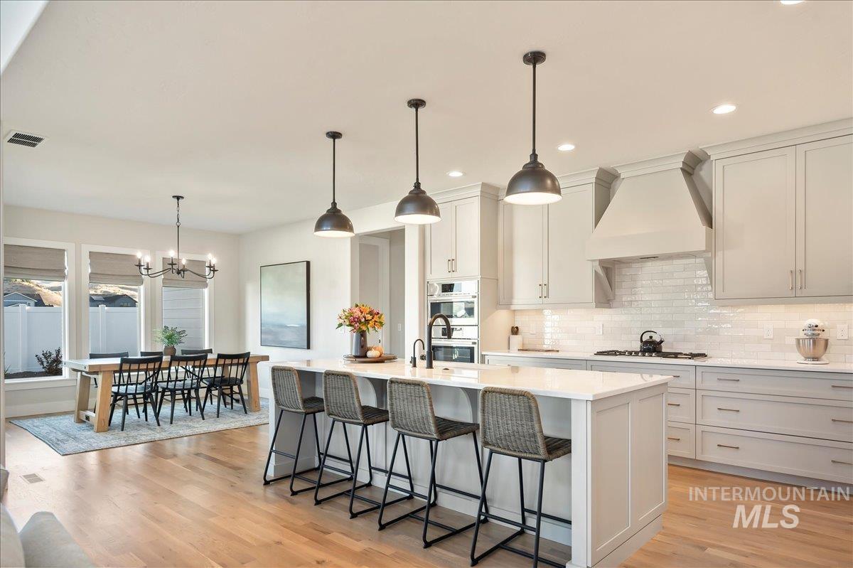 Kitchen with an island with sink, a kitchen breakfast bar, light wood-style flooring, light stone countertops, and tasteful backsplash