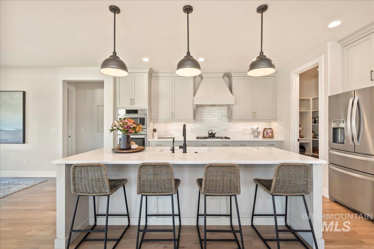 Kitchen with stainless steel appliances, light wood-style floors, decorative light fixtures, a center island with sink, and a breakfast bar