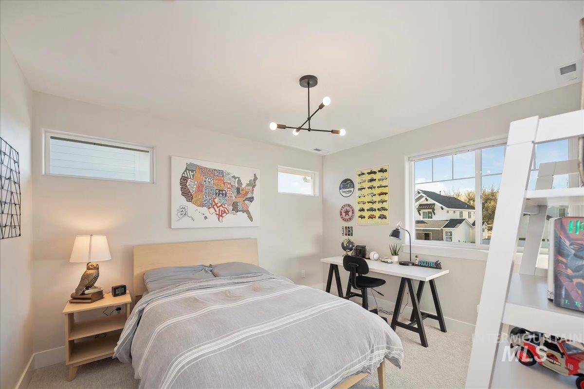 Bedroom featuring multiple windows, light carpet, and suspended lighting