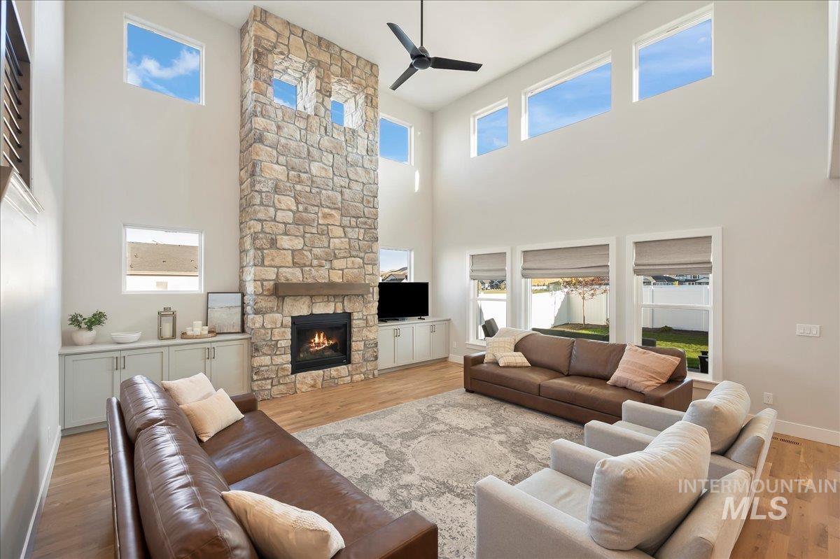 Living room with light wood finished floors, a stone fireplace, a ceiling fan, and a high ceiling