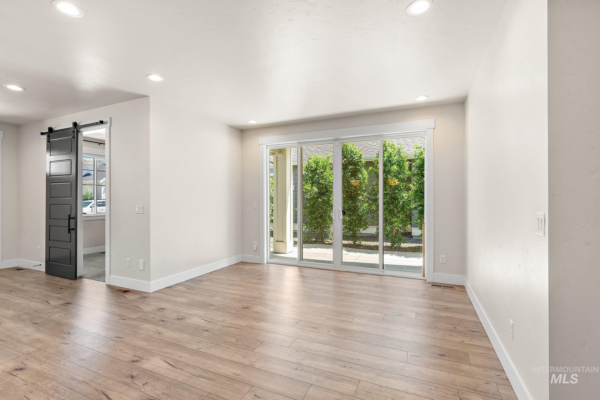 Unfurnished room with a barn door, light wood-style floors, and recessed lighting