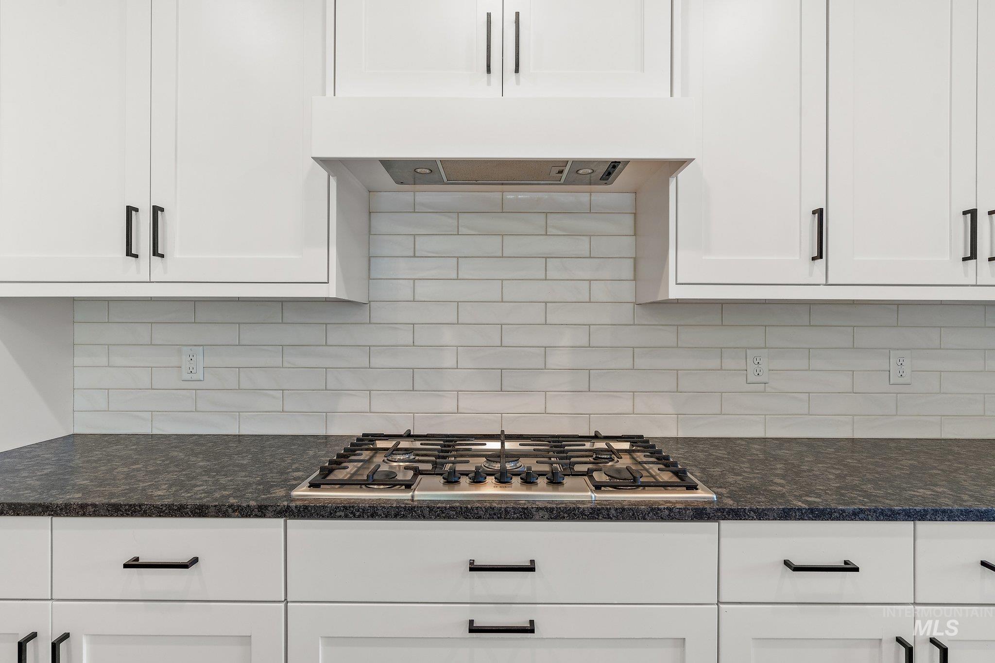 Kitchen with white cabinets, backsplash, and dark stone counters