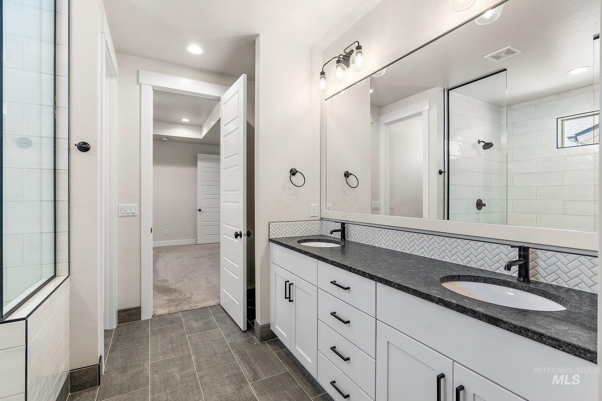 Bathroom featuring a tile shower, double vanity, recessed lighting, dark tile patterned flooring, and dark carpet