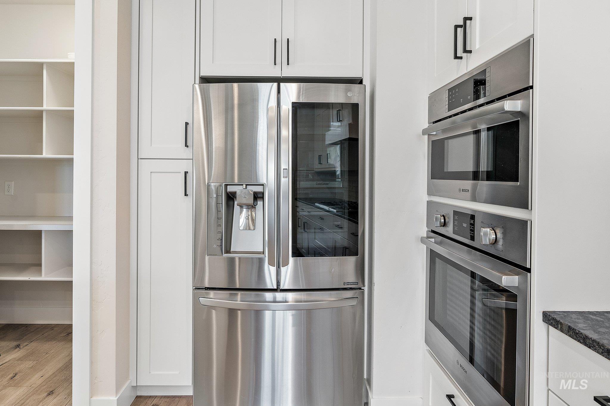 Kitchen featuring stainless steel appliances, white cabinetry, light wood-type flooring, and dark countertops