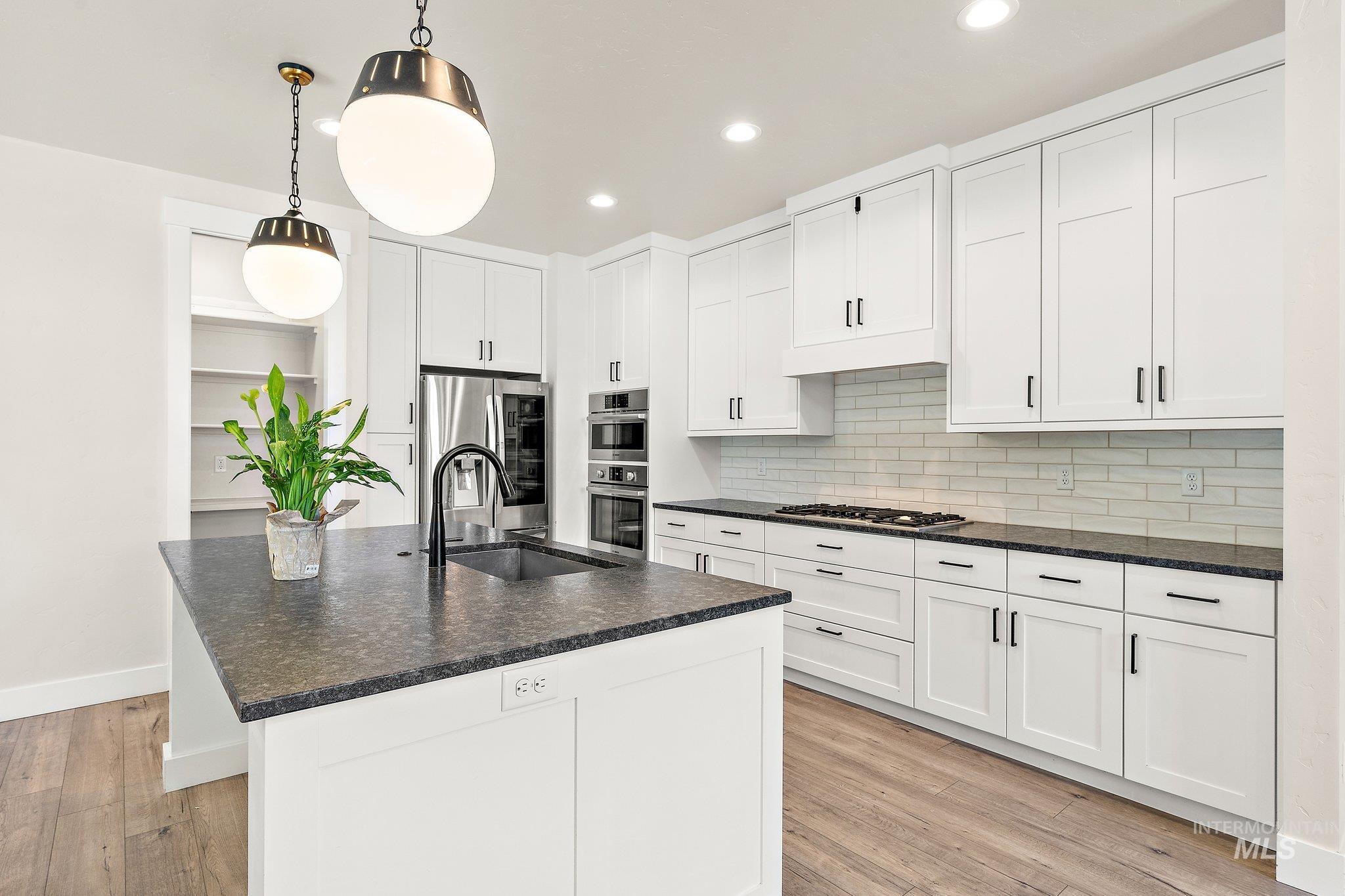 Kitchen featuring a center island with sink, pendant lighting, light wood-style floors, backsplash, and recessed lighting