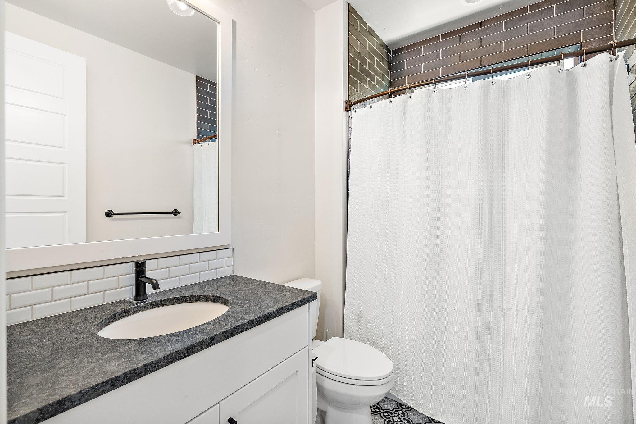 Bathroom with decorative backsplash, a shower with shower curtain, and vanity