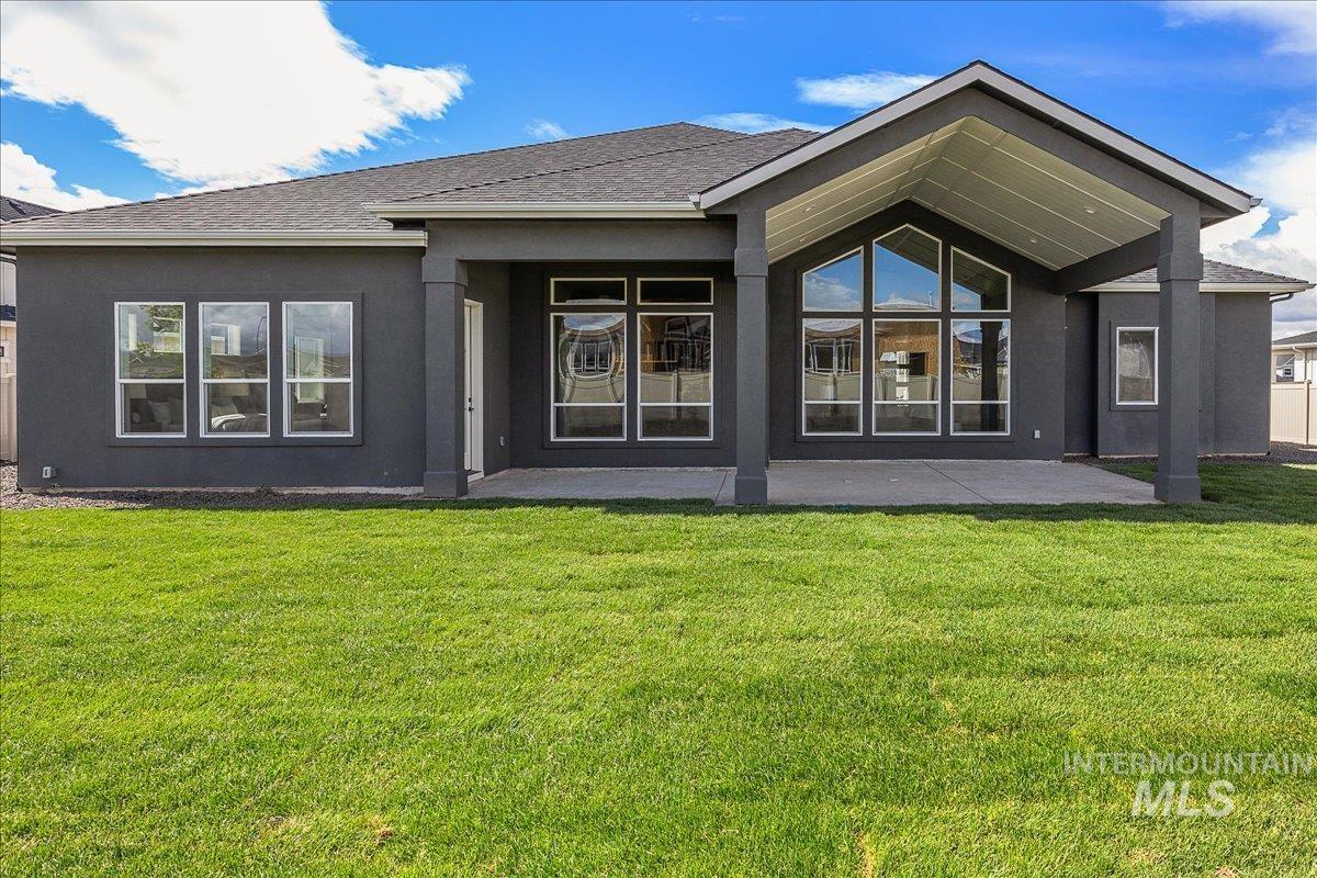 Rear view of property featuring a lawn, a patio, stucco siding, and roof with shingles