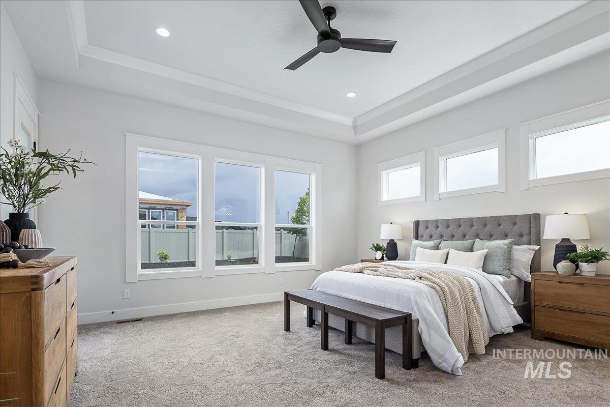 Bedroom with a tray ceiling, ceiling fan, and light carpet