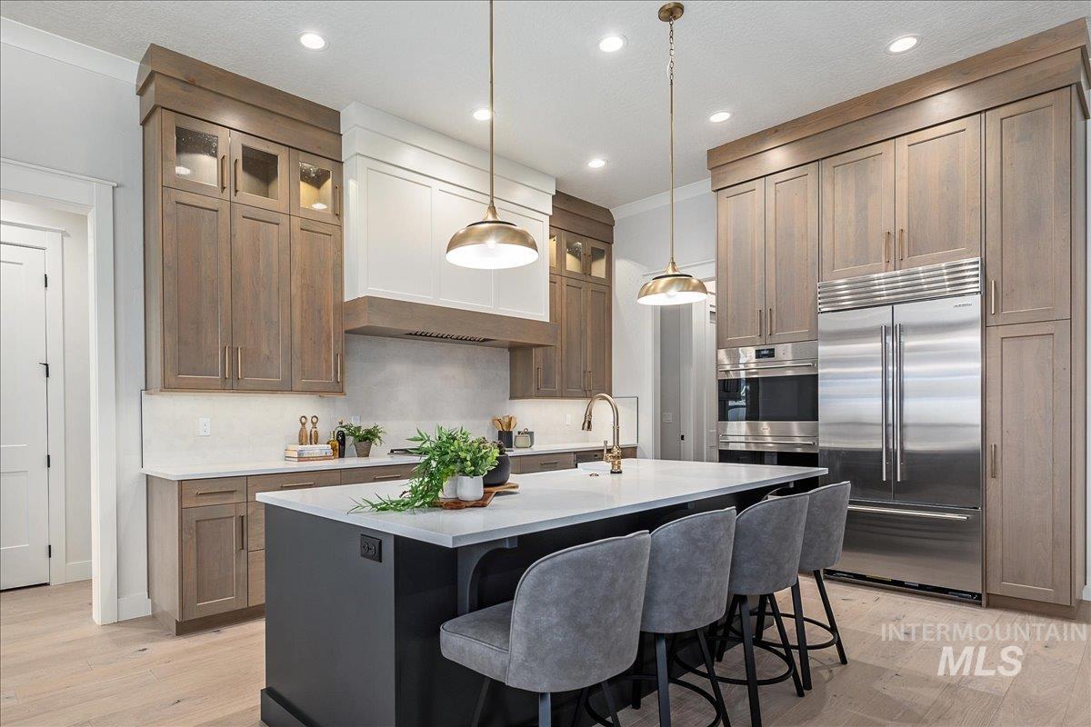 Kitchen with appliances with stainless steel finishes, a center island with sink, hanging light fixtures, light wood-type flooring, and a kitchen bar