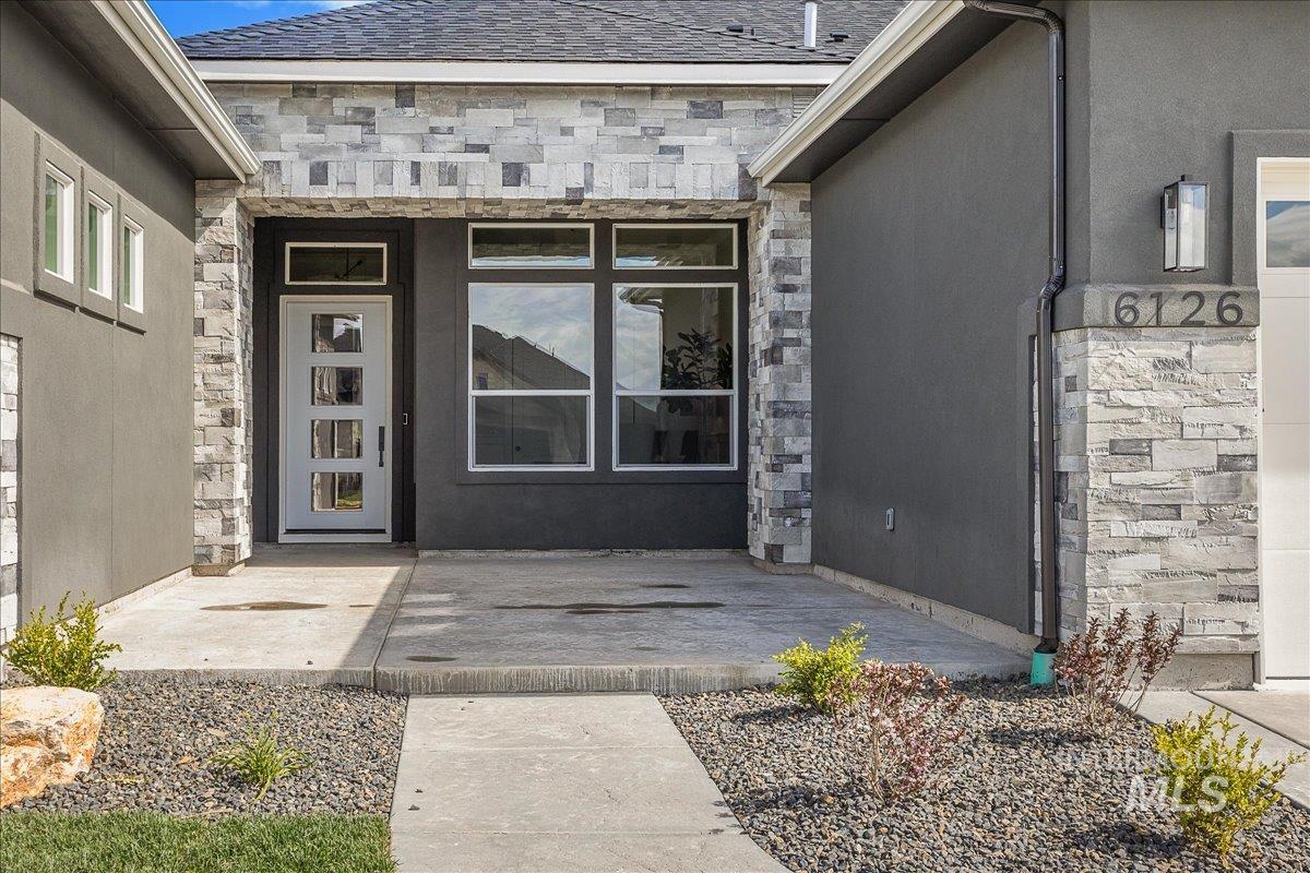 Entrance to property featuring stone siding and a shingled roof