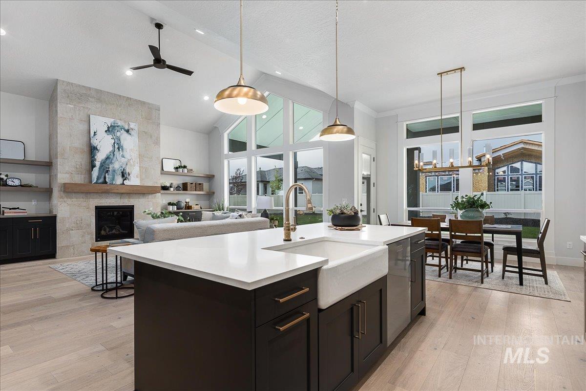 Kitchen with hanging light fixtures, open floor plan, light wood-style floors, high vaulted ceiling, and dark cabinets