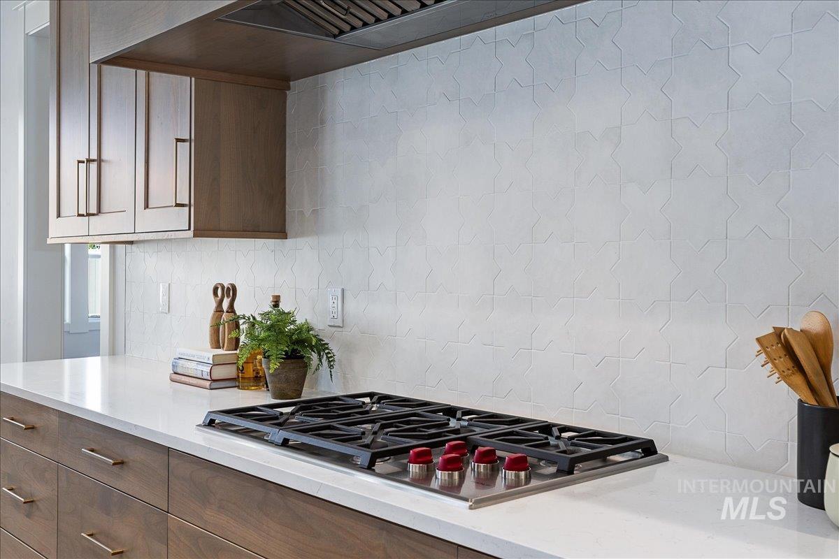 Kitchen with premium range hood, stainless steel gas stovetop, light stone countertops, and decorative backsplash
