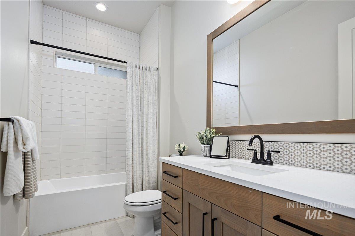Bathroom featuring vanity, shower / bathtub combination with curtain, light tile patterned floors, and recessed lighting