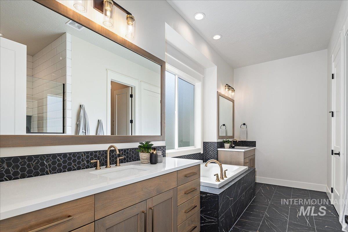 Bathroom featuring two vanities, tiled tub, and dark marble finish floors