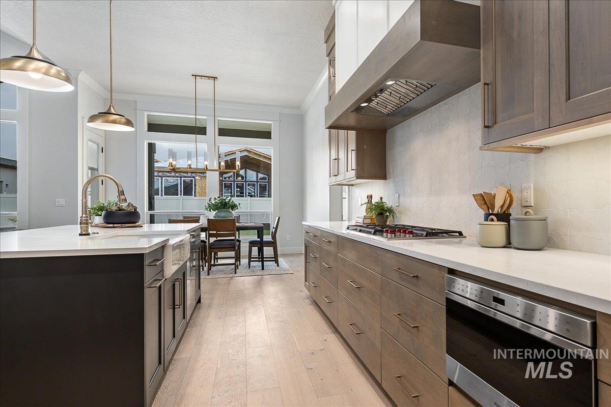 Kitchen featuring ornamental molding, extractor fan, pendant lighting, light wood-style flooring, and a center island with sink