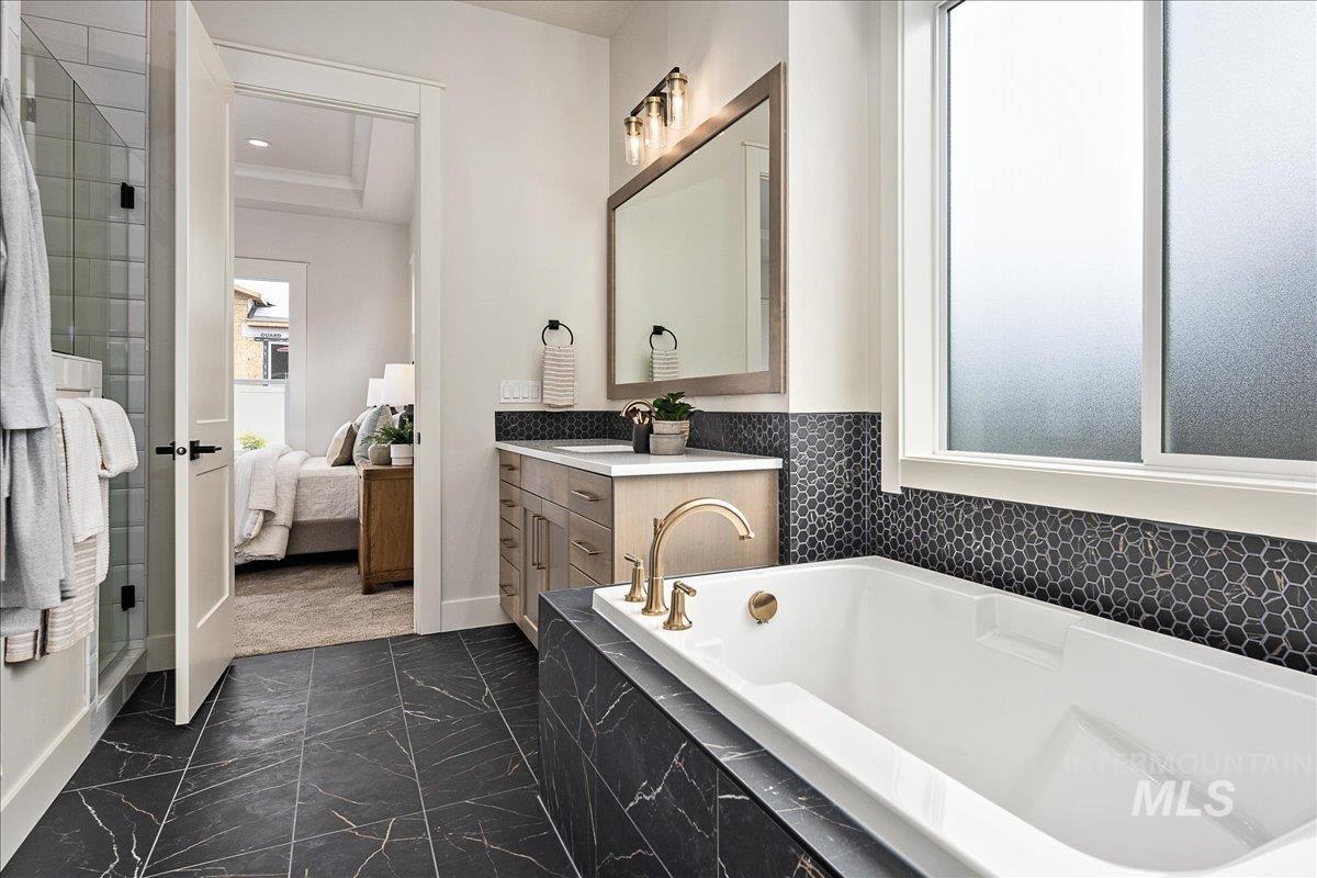 Ensuite bathroom with vanity, a bath, dark marble finish floors, and a stall shower