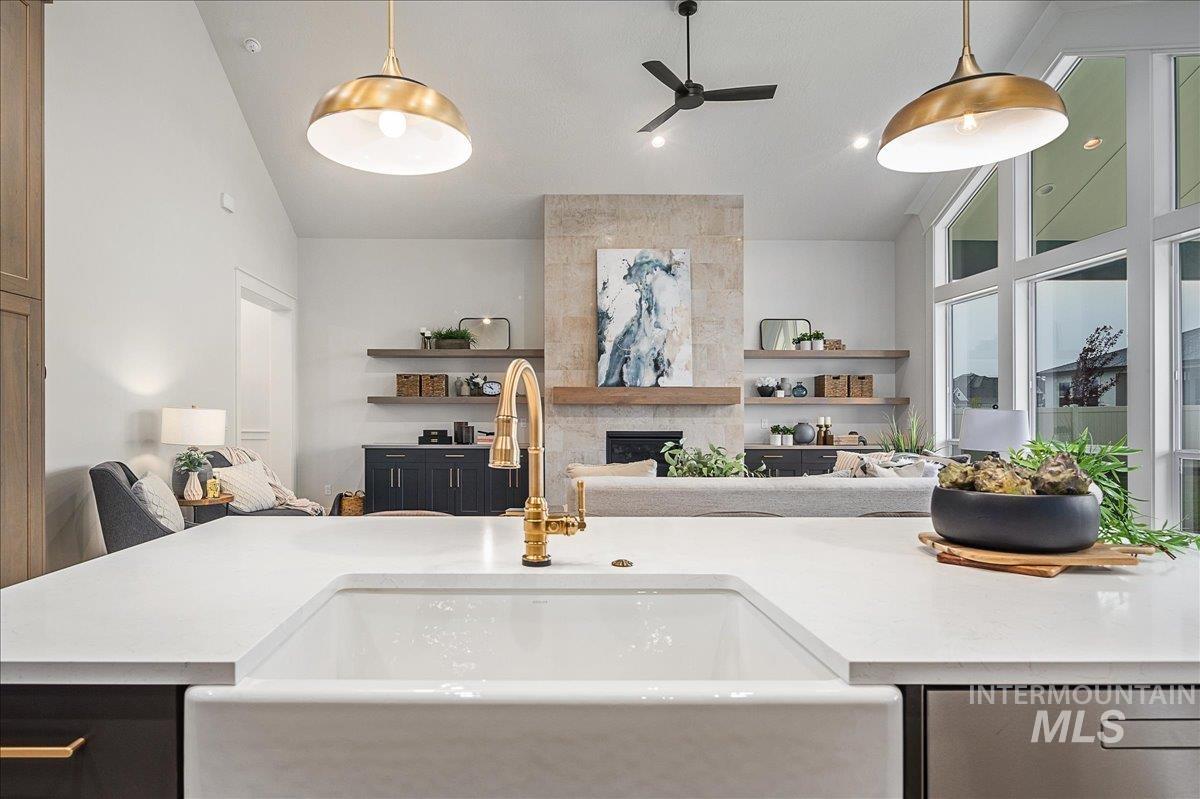 Kitchen with open floor plan, high vaulted ceiling, ceiling fan, decorative light fixtures, and a large fireplace