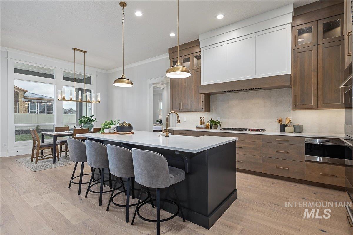 Kitchen featuring an island with sink, decorative light fixtures, a kitchen bar, ornamental molding, and tasteful backsplash