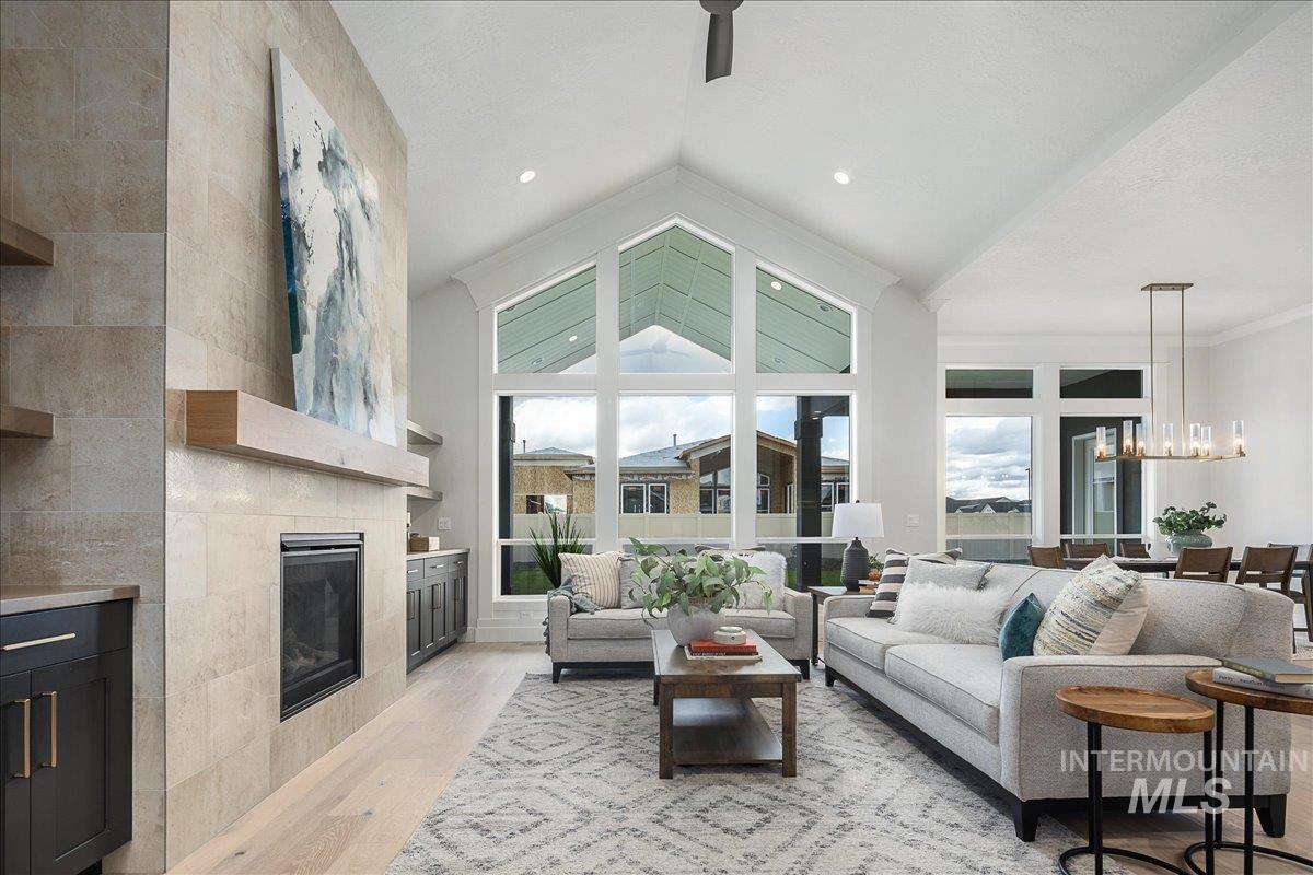 Living area featuring a chandelier, light wood finished floors, a tiled fireplace, and high vaulted ceiling