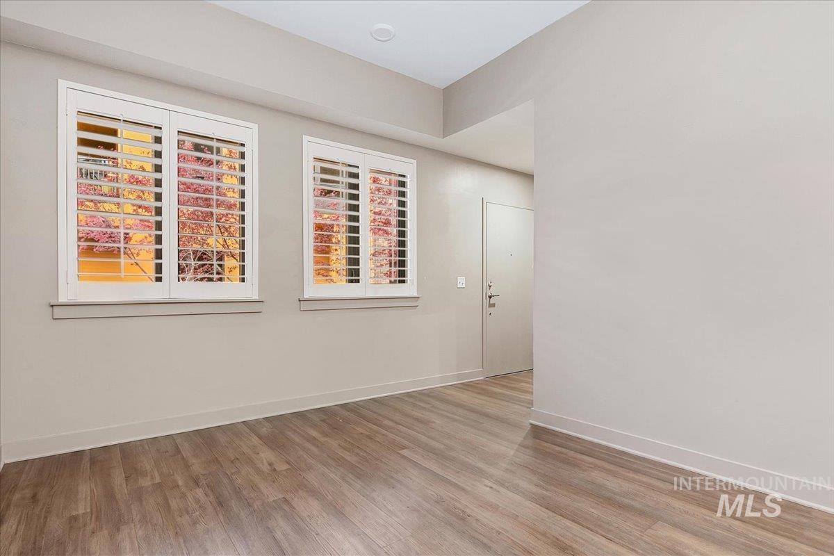 Living area featuring wood-finish flooring, light grey painted walls, and two windows with white plantation shutters