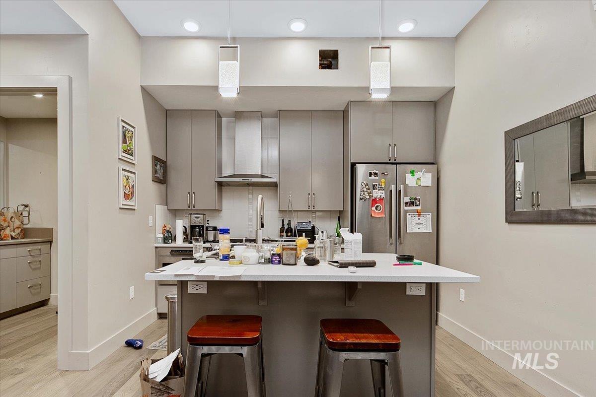 Kitchen featuring gray cabinets, a breakfast bar area, stainless steel refrigerator with ice dispenser, a center island with sink, and light wood-style floors