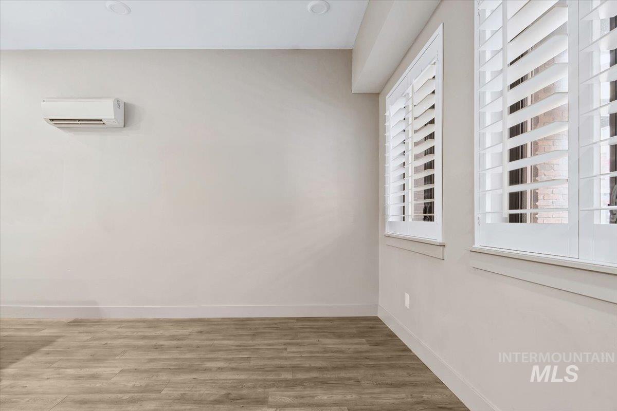 Dual windows with white plantation shutters, wood-finish flooring, recessed ceiling lighting, and a wall-mounted mini-split system