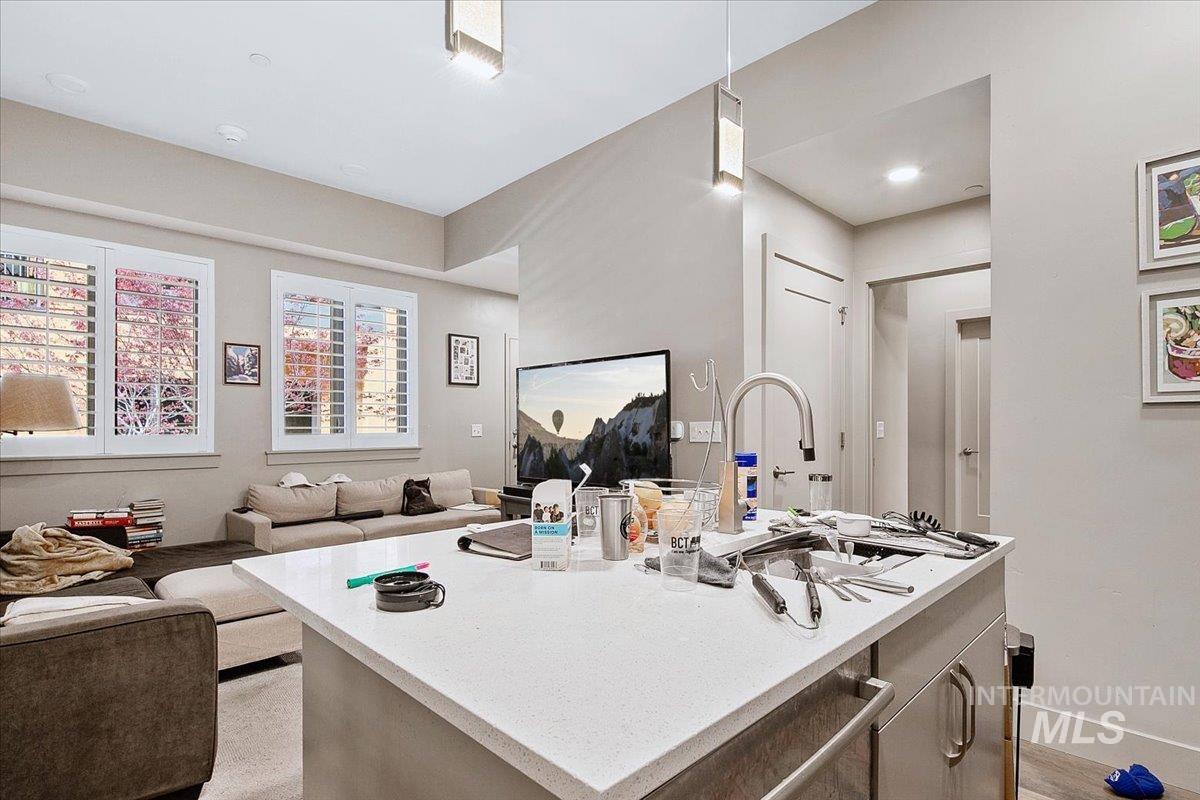 Kitchen featuring open floor plan, an island with sink, light stone counters, and decorative light fixtures