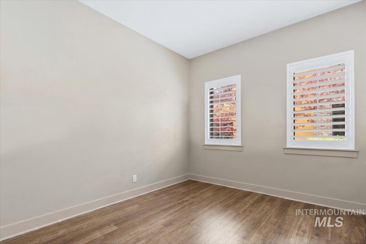 Room featuring wood-finish flooring, neutral wall paint, and two windows with white plantation shutters