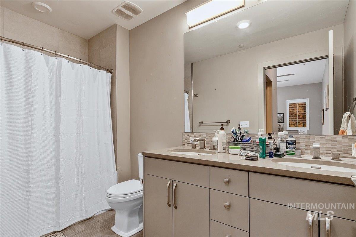 Bathroom with double vanity, curtained shower, backsplash, and parquet floors