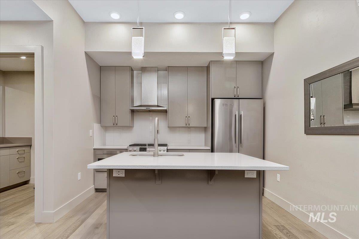 Contemporary kitchen featuring an island with a light-toned countertop, stainless steel appliances, grey cabinetry, and recessed lighting