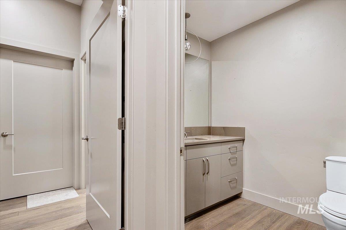 Powder room featuring a single vanity with stone countertop, undermount sink, and wood-finish flooring