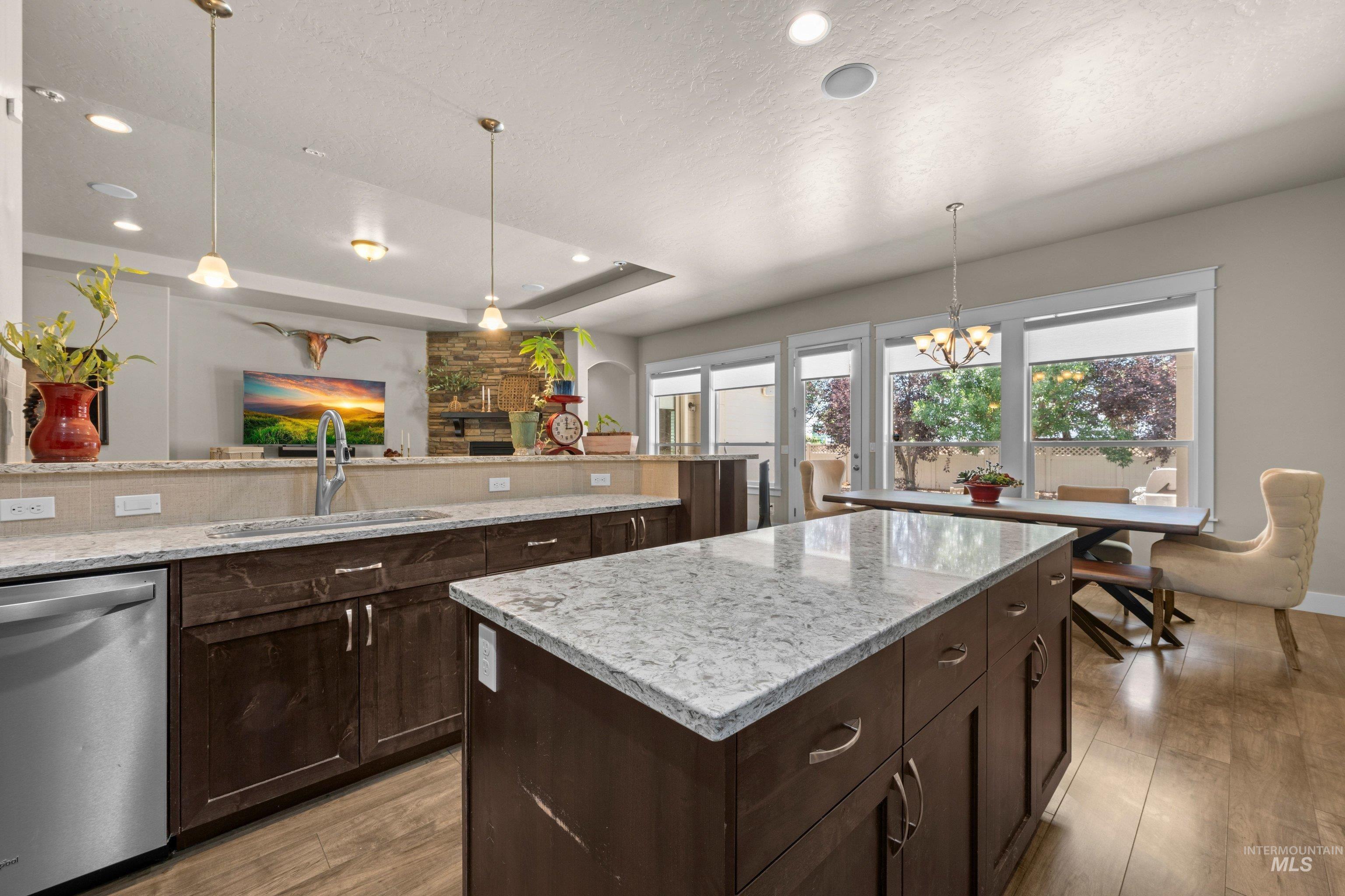 Open concept kitchen featuring an island with stone-finish countertop, dark wood cabinetry, stainless steel dishwasher, and wood-finish flooring